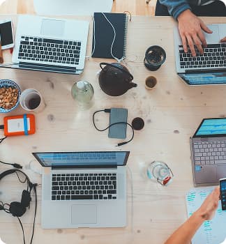 Вид сверху на четыре ноутбука, за которыми работают люди, и чашки чая на столе.